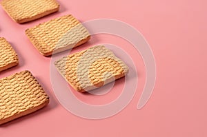 Rows of many whole square cookies lies on pink desk on kitchen