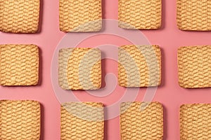 Rows of many whole square cookies lies on pink desk on kitchen