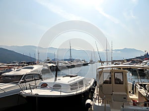 Rows of motorized pleasure and fishing boats on the pier near the city of Budva Montenegro. The background has mountains and blue