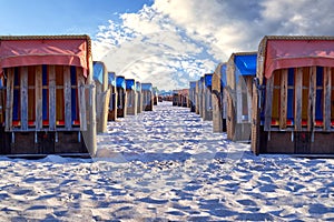 Rows of neatly placed beach chairs on the sand of a beach on the Baltic Sea under a sunny slightly cloudy blue sky