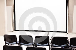 Rows of office chairs in front of a blank corporate multimedia presentation screen, vacant conference room interior, empty