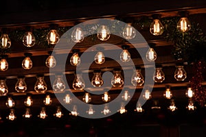 Rows of shiny golden Christmas lights on dark background. Glass bulbs with glowing filaments inside.