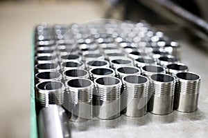 Rows of shiny metal parts with thread created on the factory with a lathe