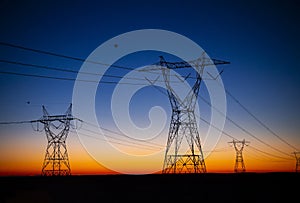 Rows of silhouetted transmission towers against dramatic desert sunset