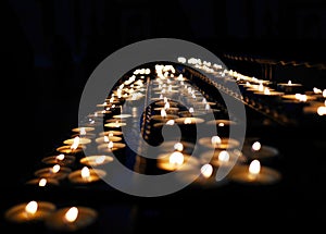 Rows of small candle lights in the dark background religion church