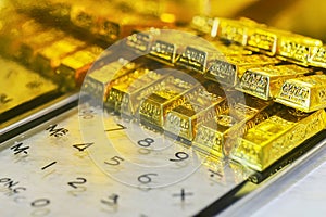 Rows of stacking gold bars with golden reflect light on transparent calculator for gold price calculating