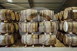 Rows of stacks of traditional full whisky barrels, set down to mature, in a large warehouse