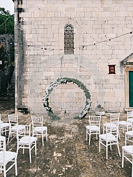 Rows of white chairs stand near the wedding arch against the wall of the old stone church