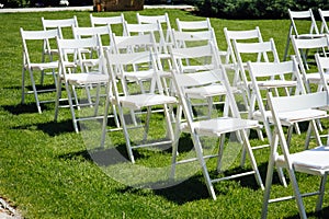 Rows of white folding chairs on lawn before a wedding ceremony in summer