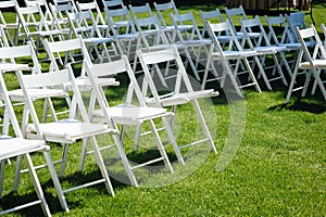 Rows of white folding chairs on lawn before a wedding ceremony in summer