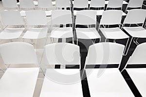 Rows of white plastic chairs for formal meetings, conference, lectures, graduation ceremonies. Room full of empty white chairs