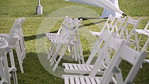 Rows of white wooden folding chairs on green lawn under a white awning.
