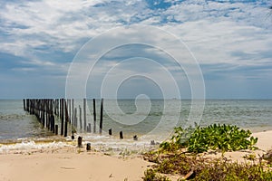 2 rows of wooden posts go out in to a calm paradise sea off of a