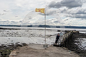 The Royal Banner of Scotland flag flying at a pier in the Firth of Forth in Culross, Scotland, UK.