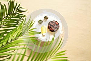 Royal dates fruit in a bowl of coconut, sunglasses, sunscreen on the white table on the sandy beach in the palm tree forest.