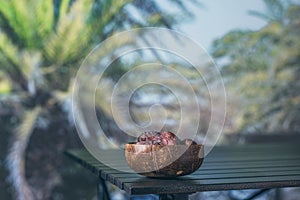 Royal dates fruit in a bowl of coconut on a table in a palm tree grove.
