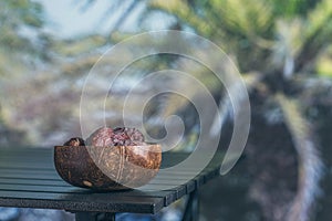 Royal dates fruit in a bowl of coconut on a table in a palm tree grove.