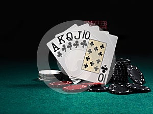 Royal flush standing leaning on colorful chips piles on green cover of playing table. Black background. Close-up.