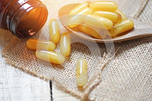 Royal jelly capsules in wooden spoon and sack background - Yellow capsule medicine or supplementary food from nature for health