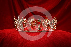 Royalty, monarch coronation or leadership conceptual idea with king gold crown with jewels on red velvet pillow photo