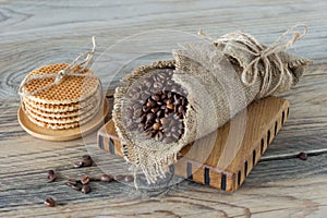 ruast arabic coffee beans in burlap with stack of dutch waffles on wooden table