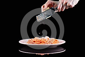 Rub grating Parmesan cheese on pasta spaghetti macaroni plate. Hands grate cheese on black background.