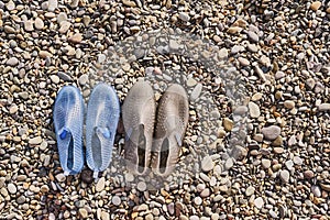 Rubber blue women`s and grey men`s slippers for swimming on a pebble beach