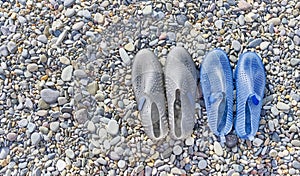 Rubber blue women's and grey men's slippers for swimming on a pebble beach
