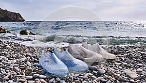 Rubber blue women's and grey men's slippers for swimming on a pebble beach