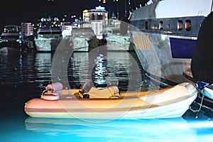 A rubber boat is moored to a yacht in the seaport. Night Scene