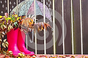 Rubber boots (rainboots) and autumnal leaves are on the wooden background with drawing umbrella. photo