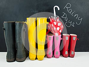 Rubber boots with an umbrella against a blackboar