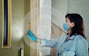 With a rubber glove, a woman in mask avoids touching an elevator button