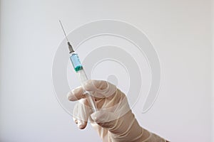 A rubber gloved hand holds a syringe filled with a blue liquid needle up
