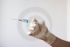 A rubber gloved hand holds a syringe with a needle filled with a blue liquid