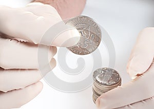 Rubber-gloved hands hold a silver American dollar on a white background