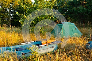 Rubber inflatable boats with fishing tackle and a tourist tent in the early morning in the fog on the river bank