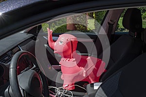 Rubber inflatable pink elephant animal toys on the front seat of a car, background with shadow reflection