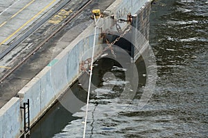 Rubber marine fender of black color and square shape attached to concrete dock with metal chain.