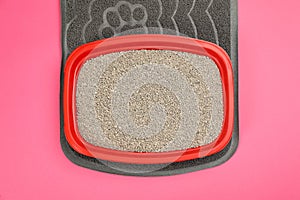 Rubber mat and cat litter tray with filler on pink background, top view