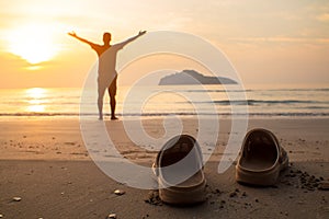 Rubber slippers on the beach with freedom the man standing, arms outstretched and watching the sunrise