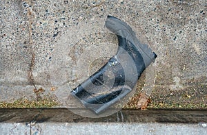 A rubber work boot laying in the gutter of a street.