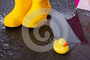 Rubber yellow boots stand in a puddle next to lies a yellow rubber duckling. bad weather