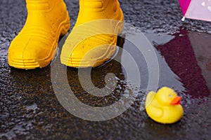 Rubber yellow boots stand in a puddle next to lies a yellow rubber duckling. bad weather