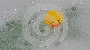 Rubber yellow duck toy floats in water in bath with foam