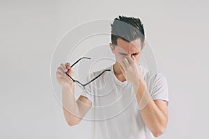 Close up portrait of an attractive man with eyeglasses. Poor young guy has eyesight problems. He is rubbing his nose and