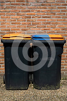 Rubbish bins for segregation plastic and paper to further recycle. Black trash cans for one household on brick wall background.