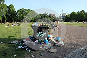 Rubbish next to rubbish bin in park with recreationists