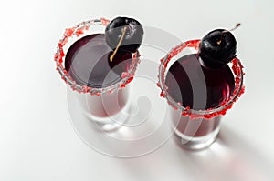 Ruby red cocktail based on vodka, cherry liqueur and syrup in drink shot glass, decorated with fresh cherry and red sugar photo