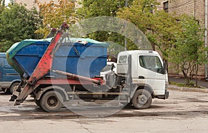 Ð¢ruck with full blue container for construction debris on board is standing outside.